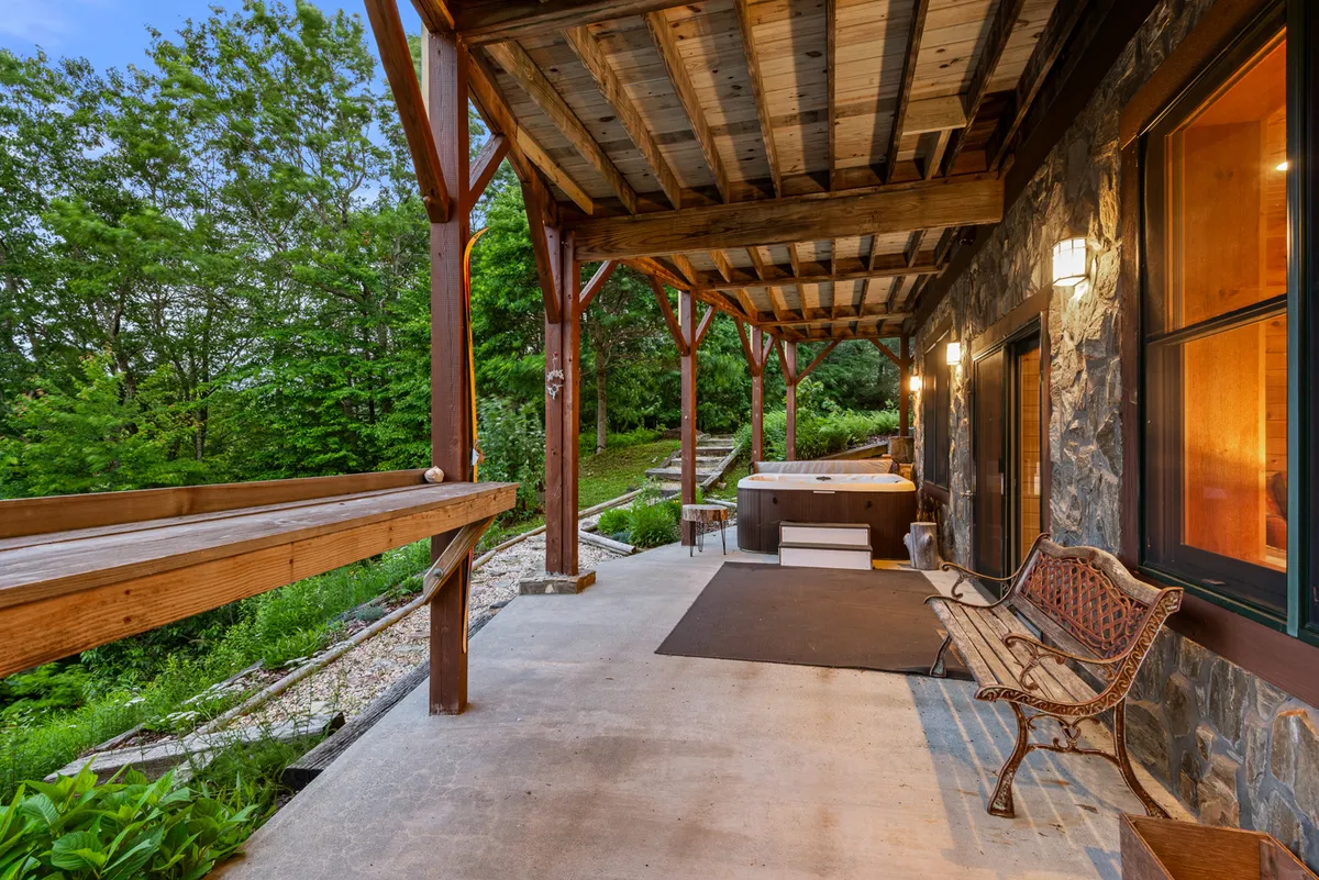 A serene exterior space featuring a hot tub and a wooden bench set against a stone wall and framed by verdant greenery. The area is designed for relaxation, with the hot tub allowing for romantic evenings under the stars and the bench providing a peaceful nook for quiet reflection or conversation.