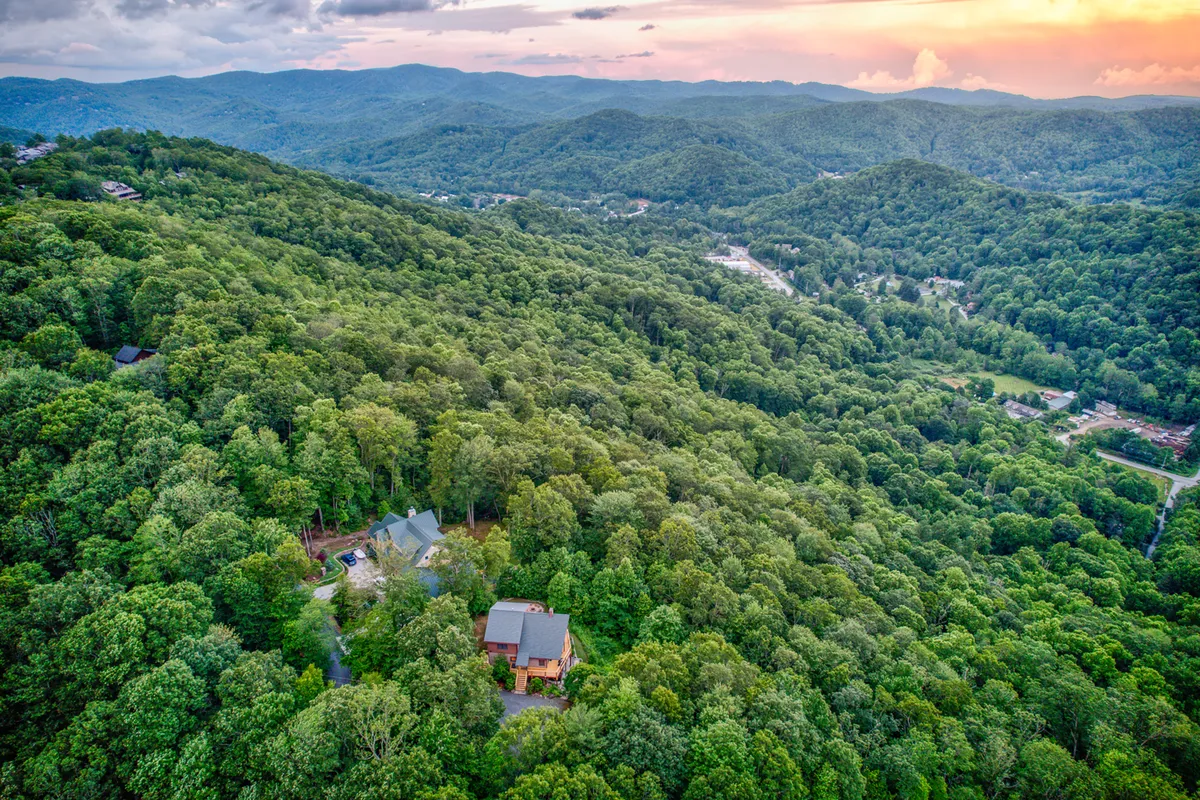 A tranquil scene of a wooden cabin nestled in a forested landscape, with a scenic mountain range and a colorful sunset sky in the background. The setting hints at endless outdoor adventures, hidden trails, and family gatherings amidst nature.