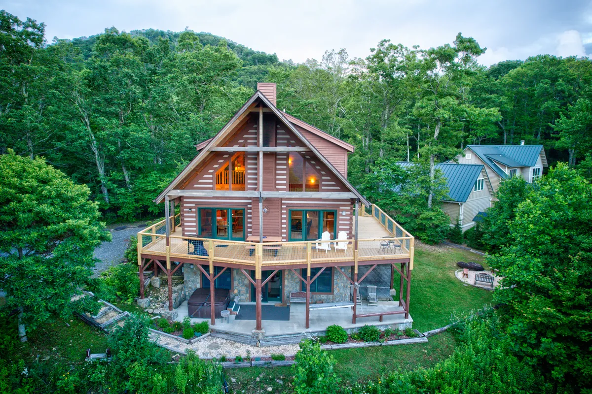 The cabin's large deck extends outward, surrounded by greenery and backdropped by rolling mountains. The expansive deck is ideal for gatherings, outdoor dining, and simply soaking up the High Country vistas at sunrise or under the stars.