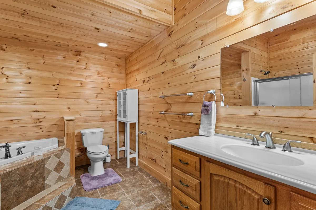 A warmly styled bathroom with wooden walls, a bathtub, a vanity with sink, and a mirror. The setting is cozy and rustic, offering a glimpse into relaxing moments after a long day of play or travel.