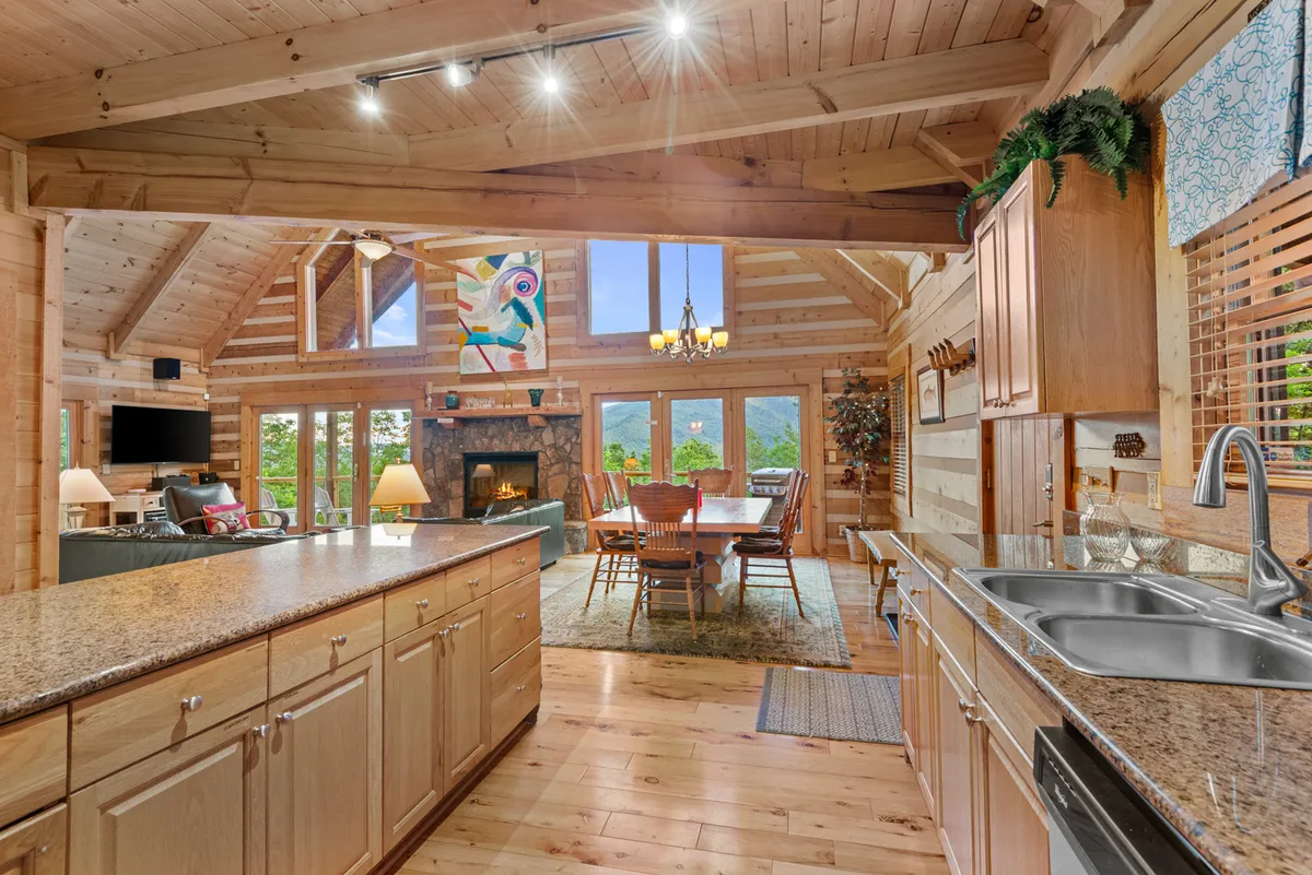 A large wooden dining table set for eight sits beside a fireplace, with large windows providing mountain views. Decorative artwork adds a creative touch. The scene is bathed in warm natural light, creating an inviting spot for family meals and games.
