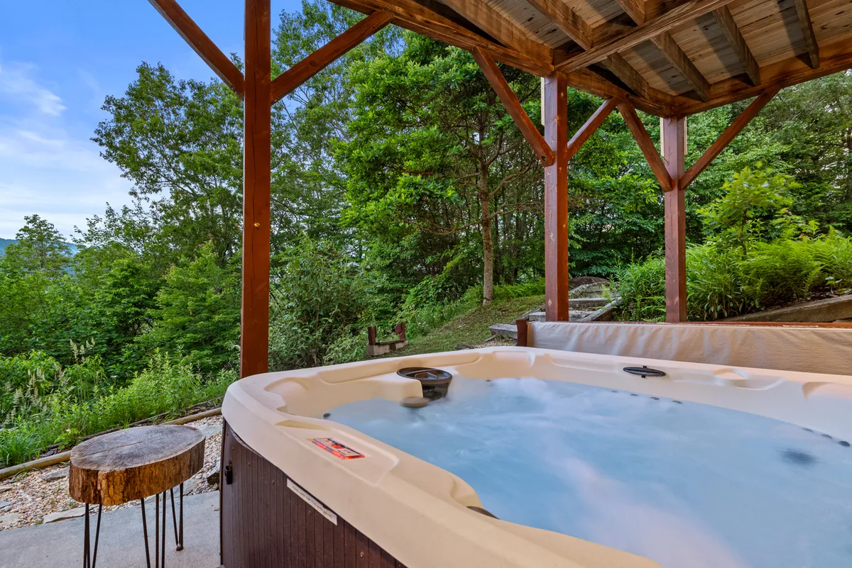 A serene hot tub area nestled beside a wooden structure, surrounded by greenery. The setting feels secluded and peaceful, perfect for unwinding with a glass of wine or stargazing in privacy.
