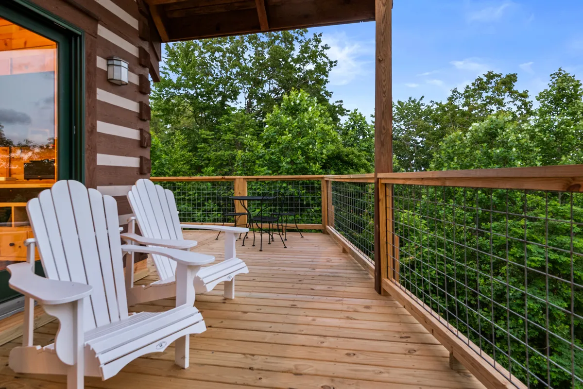 This exterior shot features white Adirondack chairs on a wooden deck surrounded by lush greenery, inviting guests to relax and enjoy the tranquility. The setup suggests a perfect spot to watch sunsets, read, or share quiet moments with a loved one while immersed in nature.