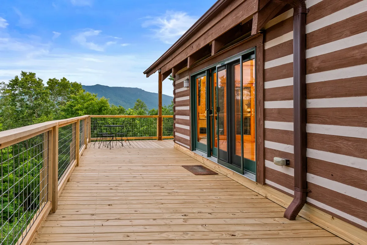 A serene shot of a spacious wooden deck overlooking a mountain view, with glass doors inviting you to step outside. The setting suggests moments of relaxation, al fresco dining, and stargazing after a day of adventure.
